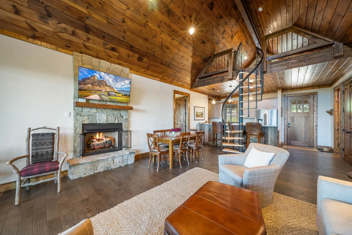This interior shot focuses on the dining area, with a sturdy wooden table set near a fireplace and a spiral staircase, creating a visually appealing, open-concept feel. The armchair and television suggest a space designed for both dining and relaxation, perfect for family gatherings or cozy evenings.