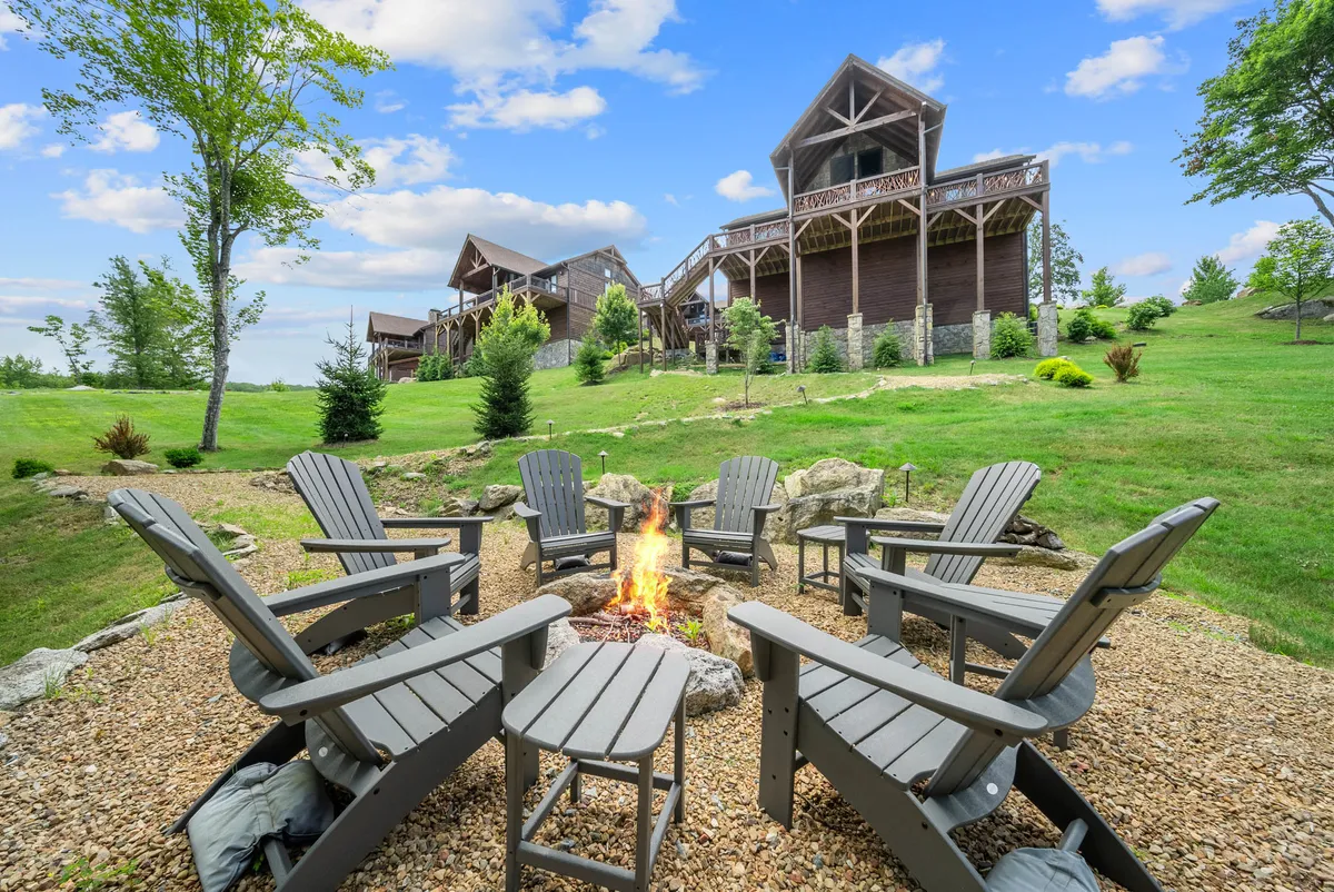 The image showcases a cozy outdoor fire pit surrounded by Adirondack chairs on a beautifully landscaped lawn, with a hint of the cabin in the background. The mountain views stretch into the distance, inviting guests to relax, share stories, and enjoy tranquil evenings under the open sky.