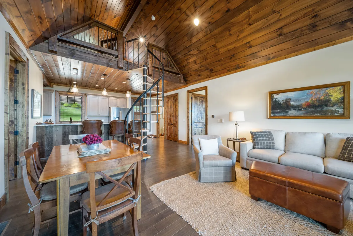 Inside, this image features a warm open-plan living area with a spiral staircase leading to the fun loft—an exciting feature for children. The dining table and cozy sofa set the stage for family meals, game nights, and relaxing together after exploring the resort's activities.
