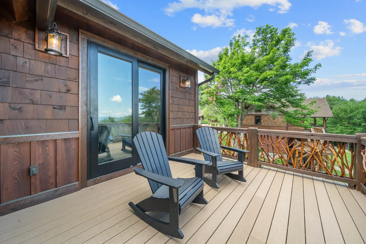 This photo highlights a charming deck with two rocking chairs, a sturdy wooden railing, and large glass doors that open to the lush, green outdoors. The setting is perfect for enjoying sunset views, morning coffee, or stargazing together. The surrounding trees reinforce the sense of privacy and connection to nature, ideal for a romantic escape.