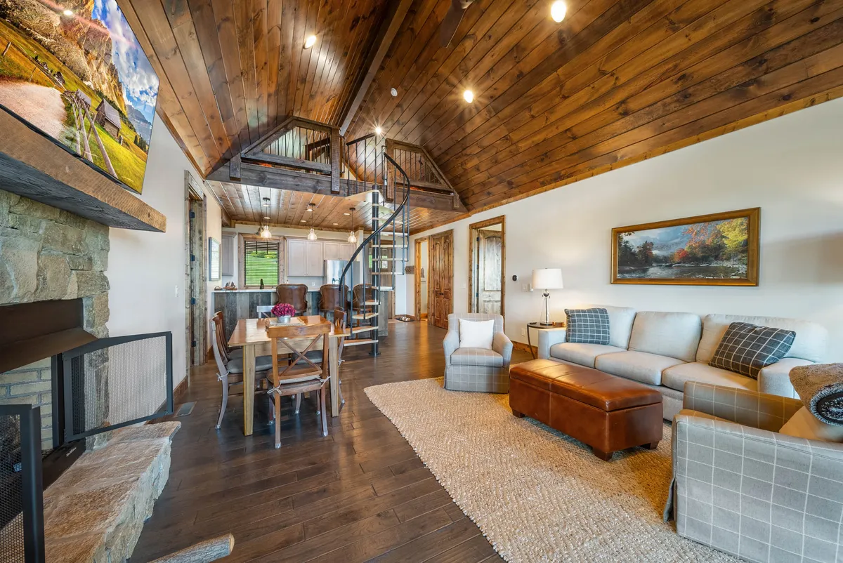 An inviting interior featuring a spiral staircase, a stone fireplace, a comfortable sofa area, and a dining table. The warm lighting and cozy textures evoke a sense of homey comfort ideal for family gatherings, game nights, or quiet evenings by the fire.