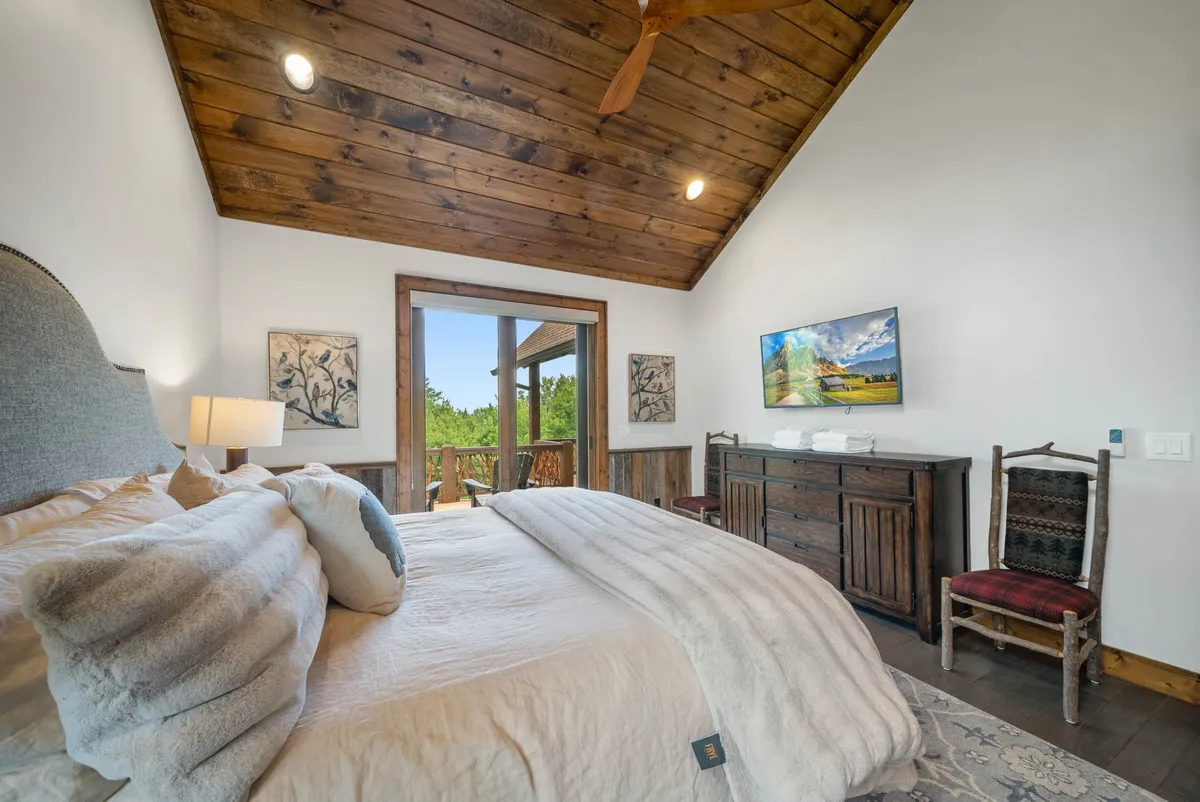 A tranquil king bedroom with plush bedding, a wooden ceiling, a large window looking out to peaceful outdoor scenery, and decorative artwork. The room exudes restful comfort, ideal for winding down after a day of adventure.
