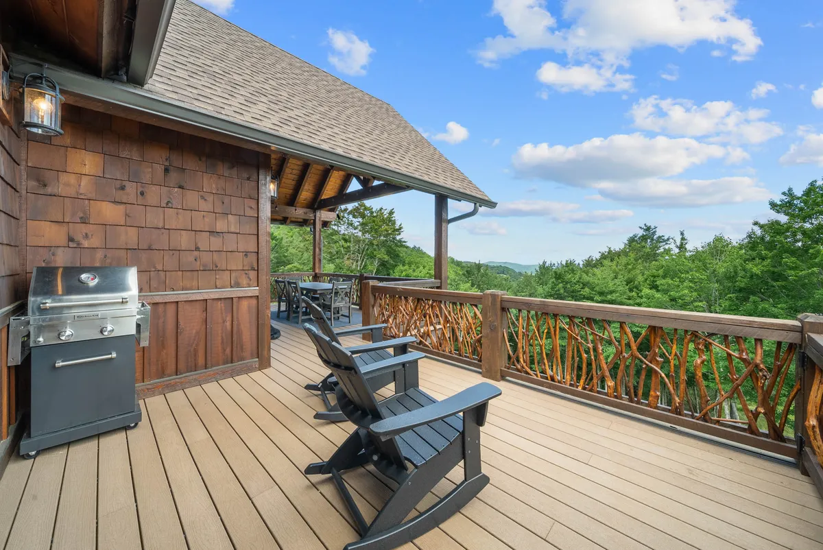 This exterior image showcases a peaceful deck space with classic wooden rocking chairs and a grill, all overlooking the surrounding natural landscape. The sturdy wooden railing frames serene views and hints at the mountain setting, inviting guests to relax outdoors after a day of adventure.