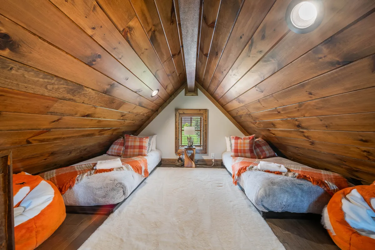A playful, inviting loft space with two twin beds under a wooden ceiling and a window offering a glimpse of the outdoors. The setup creates a cozy nook, perfect for children to relax, read, or enjoy a bit of independence while still feeling close to the main living spaces.