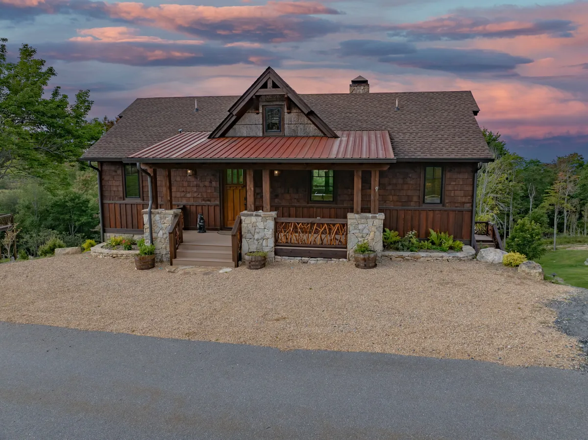 This exterior shot showcases the front porch with stone accents, wooden siding, and a landscaped area, all set against a backdrop of trees. The porch is set up for relaxing and dining outdoors, conjuring images of family evenings after a day of adventure.